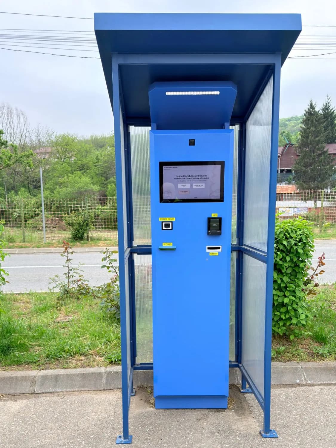RAVCOM pay station installed outdoors under a shelter, next to a road RAVCOM pay station installed outdoors under a shelter, next to a road
